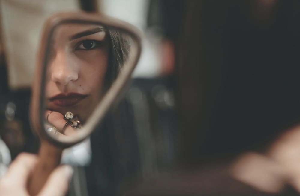 Woman looking in a hand mirror, asking why wasn't I enough during divorce