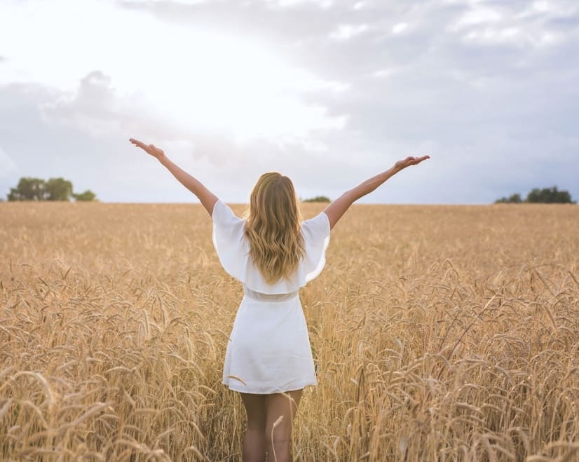 Woman raising her arms freely in a wheat field, representing the relief and freedom clients experience through EMDR and Brainspotting therapy.
